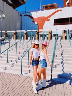 two women in cowboy hats posing for a photo on the steps at a stadium with their arms around each other