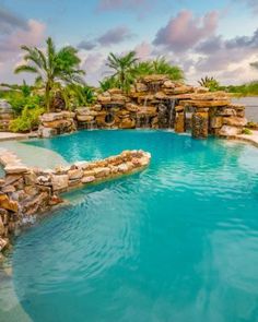 an outdoor swimming pool surrounded by palm trees and water features a waterfall that flows into the pool