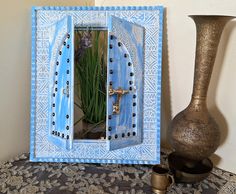 there is a vase with flowers in it next to a blue and white frame that has an open door