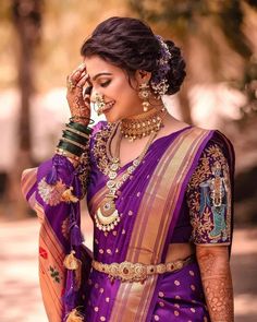 a woman in a purple and gold sari holding her hands to her face while looking at the camera