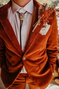 a man in an orange suit and tie with flowers on his lapel, looking at the camera