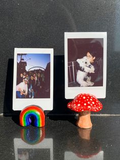 two small pictures are placed next to a mushroom on the table with a rainbow in front of them