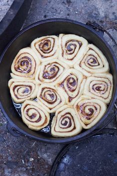 a pan filled with cinnamon rolls sitting on top of a stone floor next to an open fire