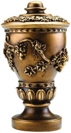 a golden vase with grapes and leaves on the top is sitting in front of a white background