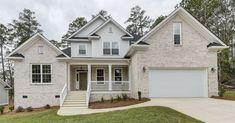 a white brick house with two car garages on the front and second story, surrounded by trees