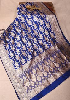 Elevate your elegance with our exquisite navy blue Banarasi katan silk saree, a true testament to timeless beauty. This stunning saree features intricate floral brocade that adds a touch of sophistication and depth to the fabric. The luxurious zari border beautifully frames the saree, enhancing its opulent charm. Perfect for weddings, festivals, or special occasions, this saree drapes gracefully, making it a standout piece in any wardrobe. Embrace the rich heritage of Banarasi craftsmanship and make a lasting impression with this captivating ensemble! SILK MARK CERTIFIED This saree is ready to wear with fall and pico done. Handmade silk tassels adorn the pallu and add more grace to it. An unstitched blouse fabric is included. *Note: There may be minor variations in the shade, the texture o Saree Drapes, Banarasi Katan Silk Saree, Silk Tassels, Katan Silk Saree, Saree Blouses, Katan Silk, Blouse Fabric, Silk Saree, Saree Designs