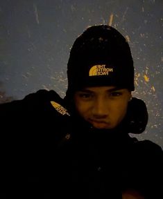 a man wearing a black hat with the north face logo on it, standing in front of a blue background