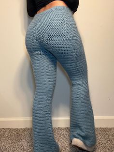 a woman in blue knitted pants leaning against a wall