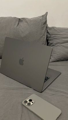 an apple laptop sitting on top of a bed next to a cell phone and pillow