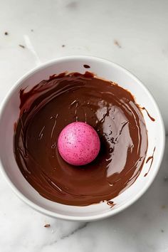 a pink chocolate egg in a white bowl on a marble counter top with melted chocolate