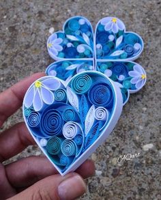 two paper heart shaped boxes are held in the palm of someone's hand, which is decorated with blue and white flowers