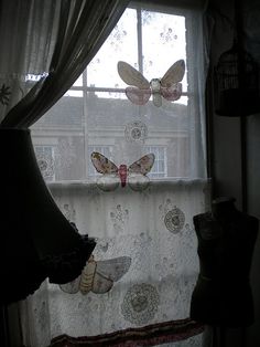 two butterflies are hanging on the window sill next to a curtain with laces