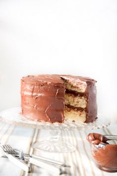 a chocolate cake with one slice missing from it on a glass plate next to two forks