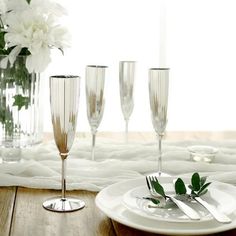 there are four champagne glasses on the table with silverware and flowers in the vase