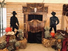 some scarecrows and hay bales in front of a wooden door with two men standing on it