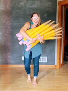 a woman in glasses holding large yellow and pink crayon pencils on her chest