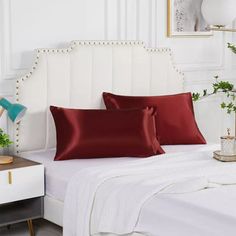 a white bed topped with red pillows next to a night stand and nightstands filled with plants