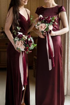 two women in long dresses standing next to each other with bouquets on their laps