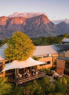 an aerial view of people sitting at tables in front of mountains with the sun setting