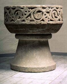 an old stone bowl sitting on top of a cement pedestal in front of a wall