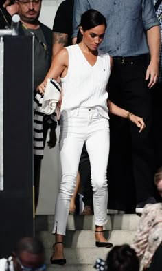 a woman in white pants and heels walking up steps with other people watching her from behind