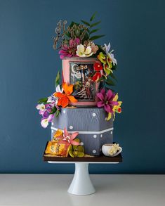 a three tiered cake decorated with flowers and books on a white pedestal against a blue wall