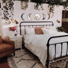 a bed with white sheets and pillows in a bedroom next to a brown chair, potted plant on the wall