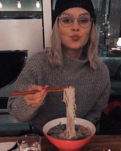 a woman wearing glasses eating noodles with chopsticks