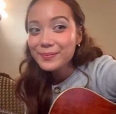 a woman holding a guitar and smiling at the camera