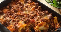 a casserole dish with meat and cheese in it on a table next to a salad