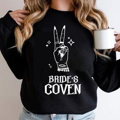 a woman wearing a black sweatshirt with the words bride's coven printed on it