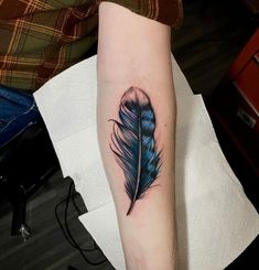 a blue feather tattoo on the arm