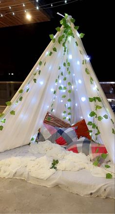 a bed covered in white sheets with green leaves on it and some lights hanging from the ceiling