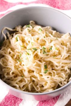 a bowl filled with noodles and parsley on top of a table cloth next to a fork