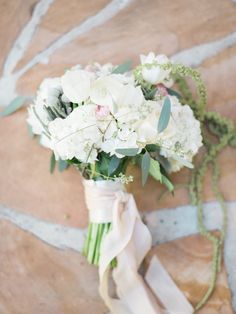 a bridal bouquet with white flowers and greenery on a stone floor in front of a brick wall