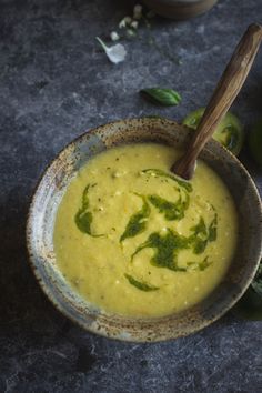 a bowl filled with yellow soup next to two green peppers and a wooden spoon in it