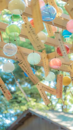 many different colored glass balls hanging from a wooden structure in front of trees and buildings