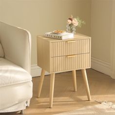 a small wooden side table with flowers on top and a book sitting on it next to a white couch