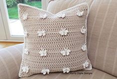 a crocheted pillow sitting on top of a couch in front of a window