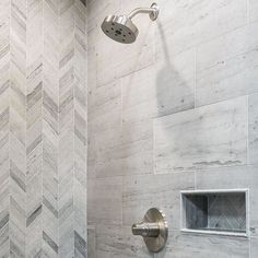 a shower head and hand shower in a white bathroom with grey herringbone tile on the walls