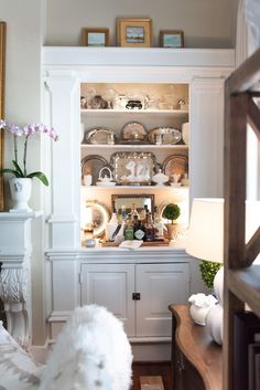 a living room filled with lots of white furniture and decor on top of wooden shelves