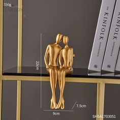 two gold figurines are standing on a black shelf next to bookshelves