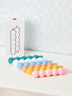 there are many different colored beads next to a card on a table with a white wall in the background