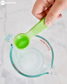 a person holding a green measuring spoon in a blender