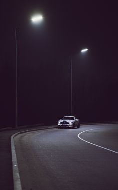 a car driving down a road at night with street lights on the side of it