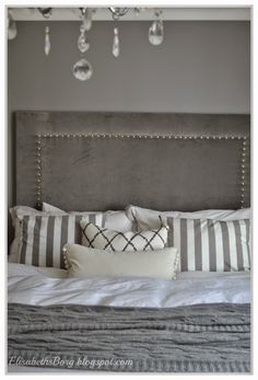 a bed with white and gray pillows on top of it next to a chandelier