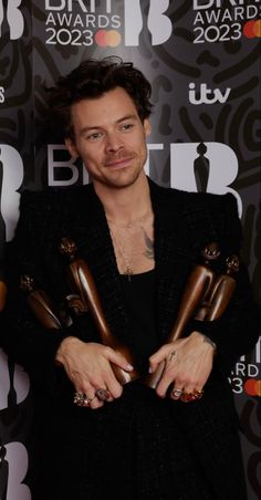 a man holding two awards in his hands and posing for the camera with one hand on his chest