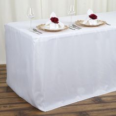 two plates with napkins on them are sitting on a white tablecloth draped over a wooden floor