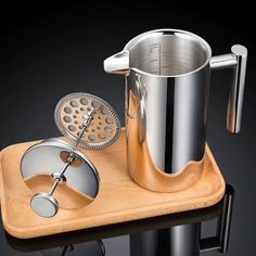 a wooden tray with a metal coffee pot and strainer on it, next to a measuring cup