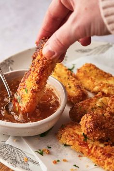 a person dipping sauce onto some fried food on a white plate with silver spoons